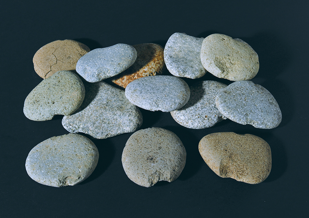 石錘：漁網用のおもりとして使用された石器。前列中央は長さ9.5cm×7.8cm